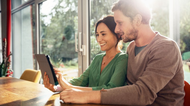 Ein Pärchen, das gemeinam am Esstisch sitzt und auf ein Tablet blicken