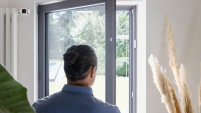 Ein Mann öffnet die Balkontür zum Lüften, daneben eine Heizung mit Bosch Smart Home Heizkörperthermostat II