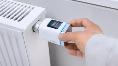 Eine Hand bedient ein Bosch Smart Home Heizkörperthermostat II an einer Heizung