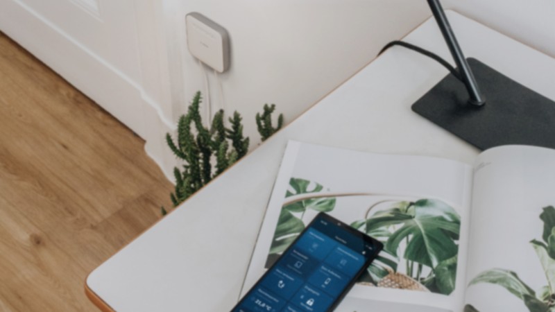 Ein Schreibtisch auf dem ein Handy liegt mit der Bosch Smart Home App und Smart Home Controller II im Hintergrund