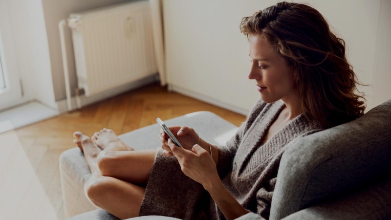 Eine Frau sitzt auf einem Sofa und hat ein Smartphone in der Hand
