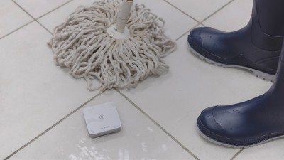 Ein Bosch Smart Home Wassermelder auf nassem Boden neben einem Wischmopp